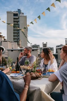 a group of people sitting around a table with food and drinks on it in front of some buildings