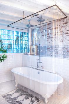 a white bath tub sitting under a window next to a plant in a room with brick walls