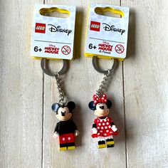 two mickey and minnie mouse keychains sitting on top of a wooden floor next to each other