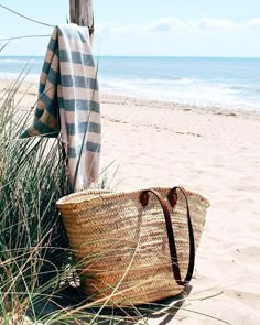 a basket and umbrella on the beach next to some grass