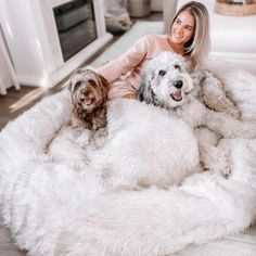 a woman is sitting on a fluffy white dog bed with two dogs in front of her