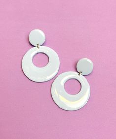 two white circular earrings on a pink background