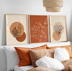 three framed art prints on the wall above a bed with orange pillows and white sheets