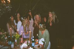 a group of women standing around a table covered in food and drinks at a party