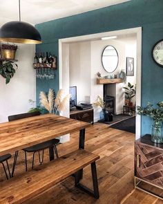 a dining room table and bench in front of a fireplace with clock on the wall