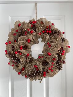 a wreath with red berries and pine cones hanging from the front door, decorated with burlap