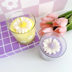 two candles and some flowers on a purple checkerboard tablecloth with pink tulips