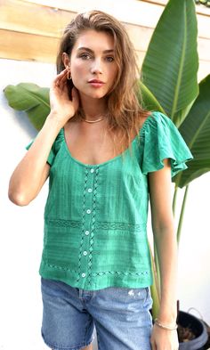 In an emerald shade, this relaxed top features a button front, lace detailing, and flutter sleeves. The lace decorations creates texture and dimension. The neckline lays in a unique way for an abstract silhouette. Flutter sleeve top Elastic sleeves Lace inserts Button front Self: 100% Cotton Length: 21 3/4" Chest: 18" Hand wash in cold water. Lay flat to dry. Low iron. Model is wearing a size small Style #: G234T6809 Bohemian Green Tops With Buttons, Bohemian Green Tops With Ruffles, Bohemian Green Blouse With Buttons, Green Bohemian Blouse With Buttons, Green Lace Top For Summer, Green Flutter Sleeve Blouse For Summer, Green Casual Lace Top, Green Casual Blouse With Lace Top, Summer Ruffle Sleeve Tops With Buttons