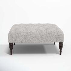 the footstool is made from wood and has a light gray upholstered fabric