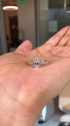 a person's hand holding a ring with a diamond on it, in front of a glass door