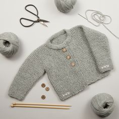 a knitted sweater and knitting needles on a white surface with yarn balls, scissors and thread