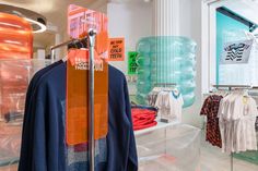 an assortment of clothing on display in a store with orange and blue banners hanging from the ceiling