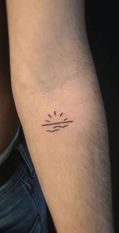 a man's arm with a small sun and waves tattoo on the left inner arm