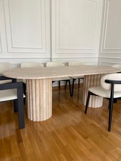 a dining table with chairs around it on a hard wood flooring area in a white walled room