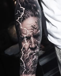 a man's arm with a black and grey tattoo on it, depicting the face of an old man