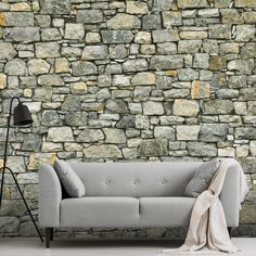 a couch sitting in front of a stone wall with a blanket on top of it