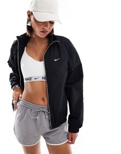 a woman in grey shorts and a white hat wearing a black jacket with the nike logo on it