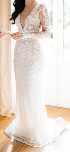 a woman in a white wedding dress standing on a wooden floor next to a window