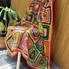 a colorful crocheted blanket sitting on top of a wooden chair next to a potted plant