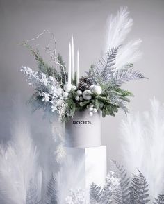 a white cake with frosting and greenery on top is surrounded by feathers, pineconis, berries, and candles