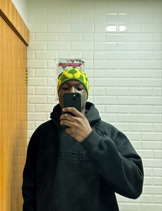 a man taking a selfie in front of a mirror wearing a yellow and black hat