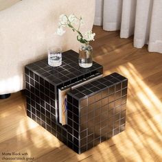 a black and silver side table with a vase on it next to a white couch