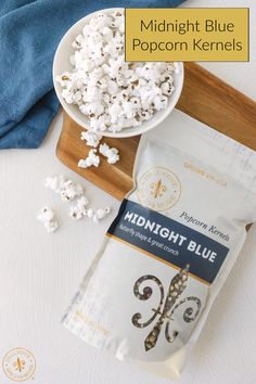 a bag of popcorn next to a bowl of popcorn on a cutting board with the words midnight blue popcorn kernels