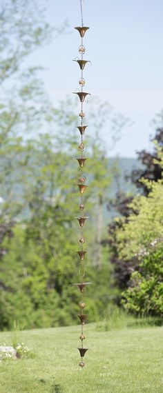 a tall metal sculpture sitting on top of a lush green field with trees in the background