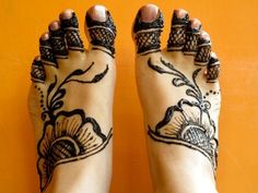 a woman's feet with henna tattoos on their ankles and toes, against an orange wall