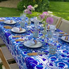 a blue and white table cloth with flowers in vases on it, along with plates and utensils