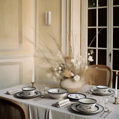 a table set with plates, silverware and a vase filled with flowers on it