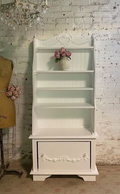 a white bookcase sitting next to a mannequin with flowers in it on display