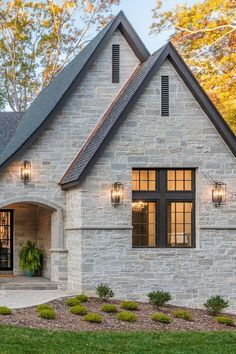 a brick and stone house with black shutters on the front door is shown in autumn