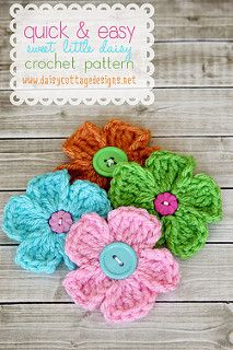 crocheted flowers with buttons on them sitting on a wooden surface