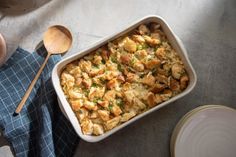 a casserole dish with bread and vegetables in it next to two wooden spoons