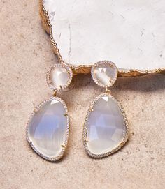 Featuring abstract ovals crafted from warm brass, each of these earrings is adorned with genuine moonstones that exude a twinkling cat's eye glow, adding a touch of mystery and allure to your look. The unique design brings a modern edge to the classic combination of brass and moonstone, making these earrings a perfect accessory for those who appreciate both sophistication and trendsetting style. Drop: 2.0" Width: 1.5" Weight: 0.05 lbs Plated Made of brass and cubic zirconia Cat's eye stone finis Modern Moonstone Earrings As Gift, Teardrop Moonstone Earrings With Gemstone Accents, Elegant Gold Crystal Earrings With Moonstone, Moonstone Drop Earrings With Gemstone Accents, Elegant Moonstone Teardrop Earrings, Elegant Moonstone Earrings With Gemstone Accents, Elegant Teardrop Moonstone Earrings, Modern Oval Moonstone Jewelry, Modern Moonstone Drop Earrings