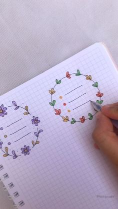 a person is writing in a notebook with flowers on the page and a wreath drawn on it