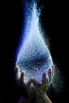 a person holding their hands under a water drop in the dark with blue light coming from them