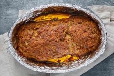 a baked dish in tin foil on top of a table with a napkin and fork