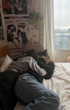 a person laying on top of a bed in front of a window next to a wall with posters