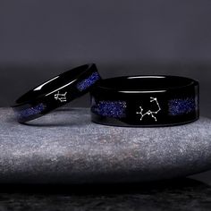 two black ceramic rings with blue glitter inlays on top of each other, sitting on a rock