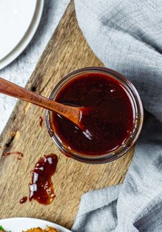 a wooden spoon sitting in a jar filled with ketchup next to a plate of food