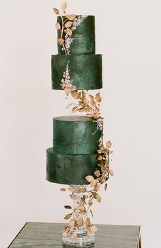 a three tiered green wedding cake with gold leaves on top