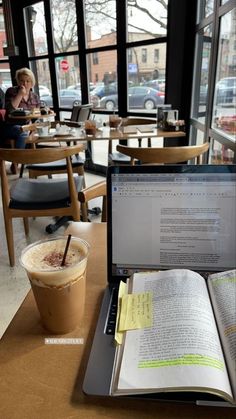 an open book sitting on top of a laptop computer next to a cup of coffee