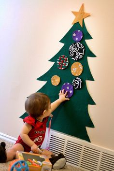 a small child reaching up to decorate a christmas tree on the wall with other children's toys