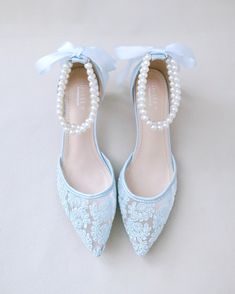 a pair of blue shoes with pearls and bows on the toes are sitting on a white surface