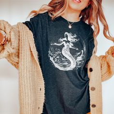 "We love this fun, colorful unisex Vintage Mermaid in White design T-shirt! This tee is soft and super comfy and is made of 100% cotton. Heather tees are a soft cotton-poly blend. We use BELLA+CANVAS for our T-shirts! FABRICATION * Solid Colors: 100% Ringspun Cotton * Heather Colors: 52% cotton, 48% polyester * Runs true to size SIZING This style is a unisex t-shirt. If you are unsure about the size you should order, please refer to the size chart in the pictures. CARE INSTRUCTIONS * Machine wash: warm (max 40C or 105F) * Tumble dry: low heat * Do not iron directly on print * Do not dryclean PRODUCTION TIME / SHIPPING TIME *Please click the \"Shipping and Policies\" tab under each listing photo to view our current production time. Note: these are custom items that are printed when ordered. Mermaid Mom Shirt, Mom Mermaid Shirt, Mermaid Shirts, Sleeping With Sirens Shirt, Mermaid Vinyl Shirt, Mermaid Tshirt, Mermaid Shirt, Vintage Mermaid, Vintage Shirt