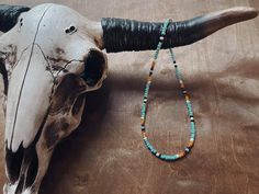 an animal skull with long horns and beads on it's neck is displayed in front of a wooden table