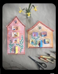 two paper houses sitting on top of a table next to scissors and flowers in a vase