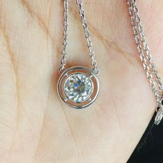 a close up of a person's hand wearing a necklace with a diamond on it